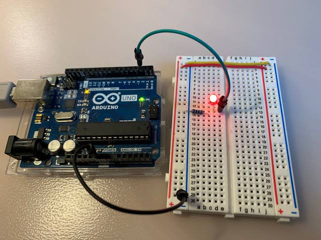 Carte programmable avec un capteur branché et une LED allumée, posée sur une table de classe à côté d'un ordinateur portable